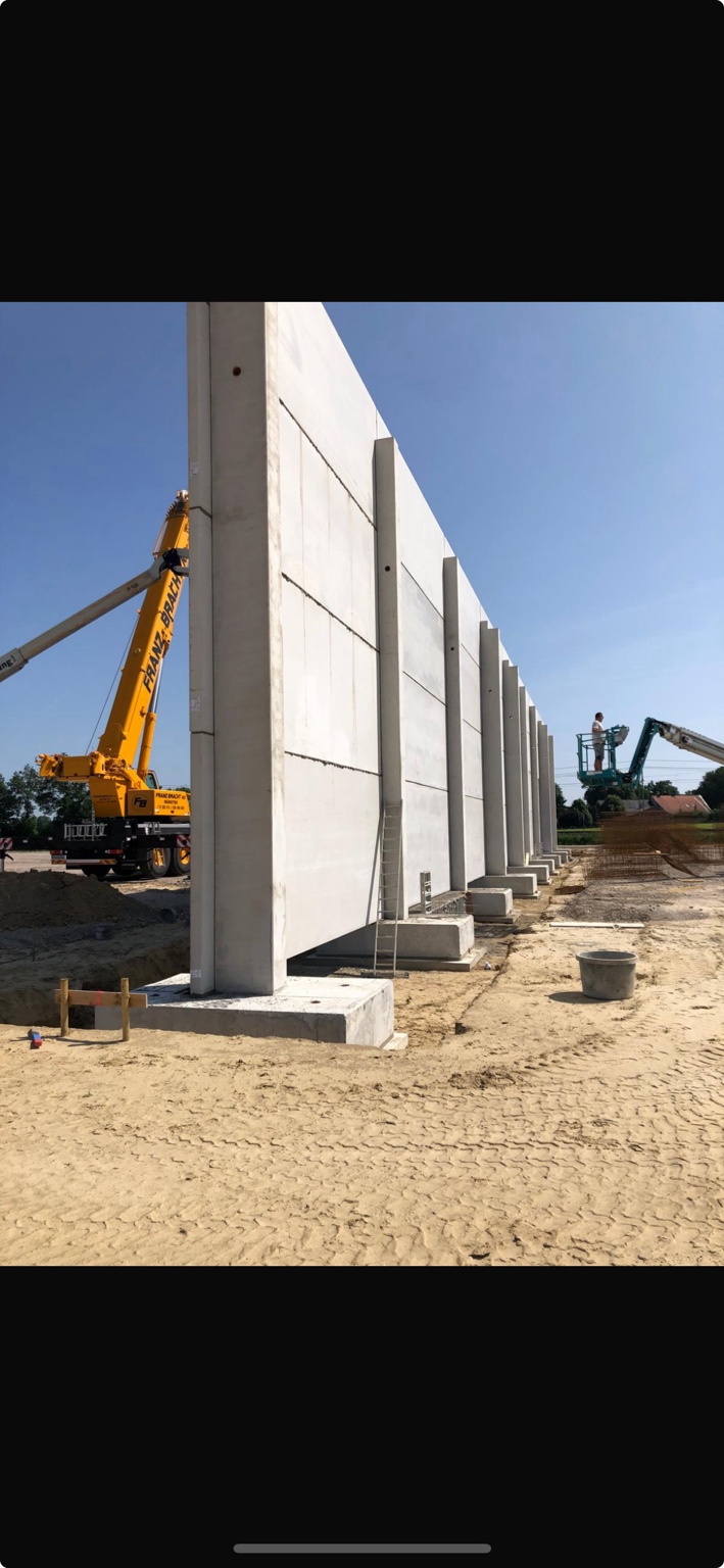 Montage langer Betonfertigteilwände mit Kran und Arbeitsbühne